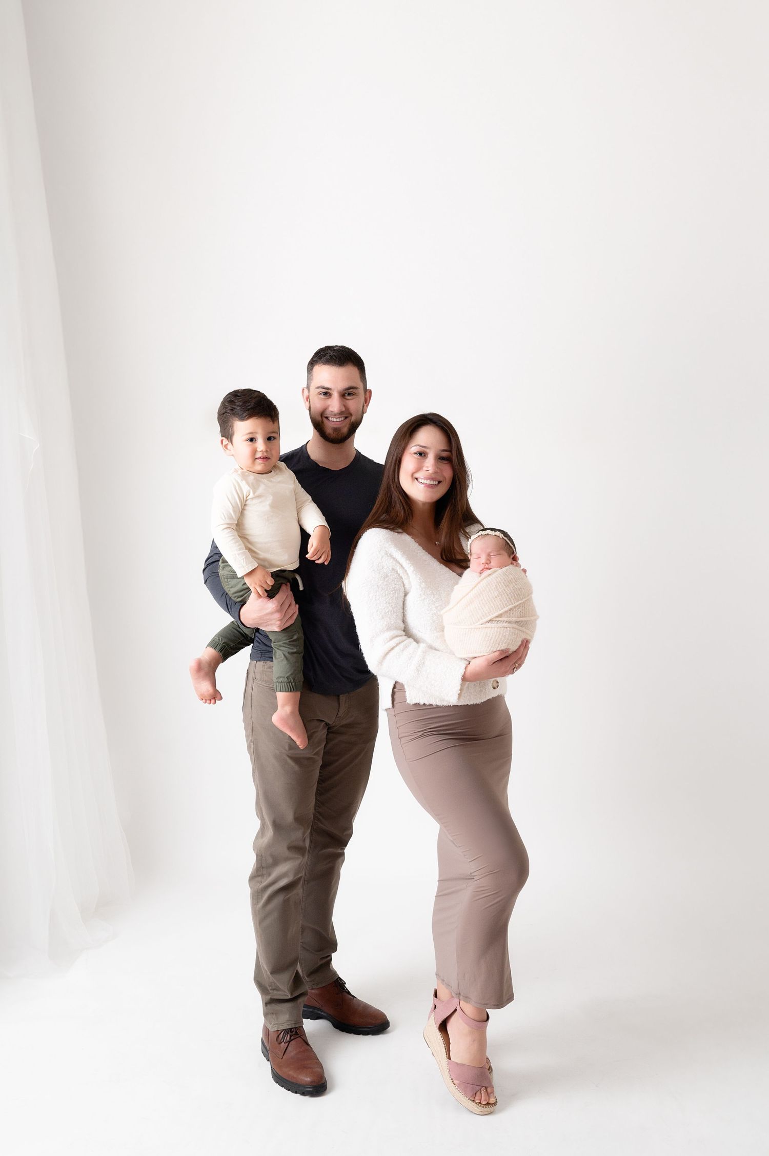 A family of four poses together against a white backdrop in coordinated neutral-toned outfits.