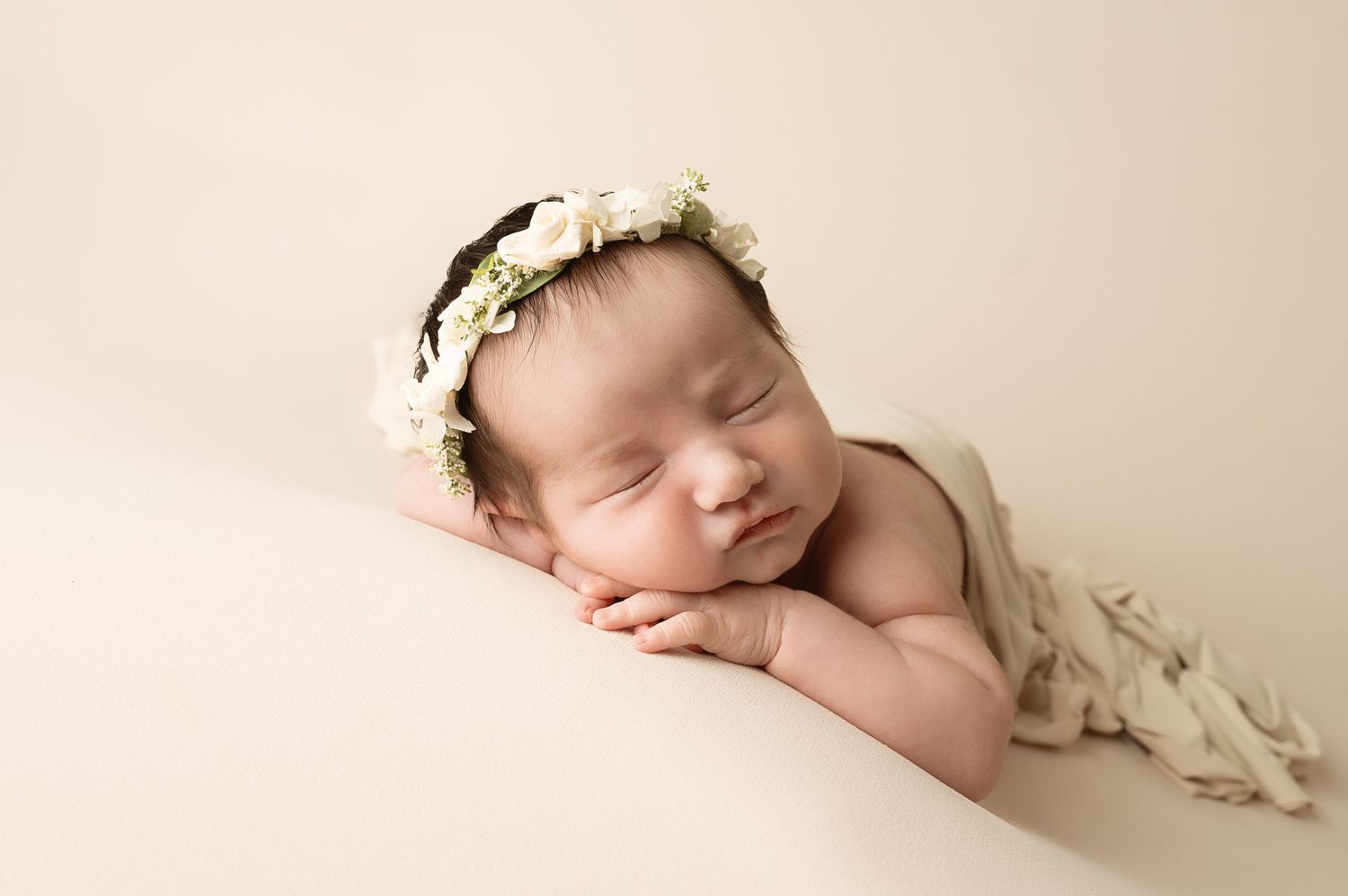 Artistic newborn photography with neutral tones and floral headpiece details.