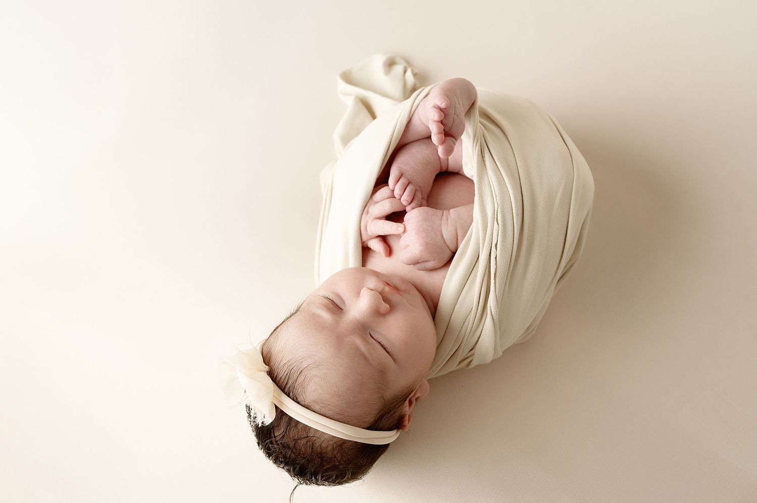 Artistic newborn studio portraits with soft cream colored wraps and backdrops.