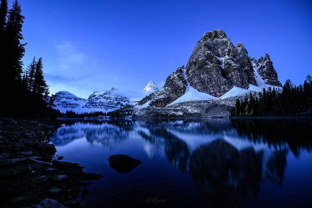 Mount Assiniboine reflects perfectly in a calm alpine lake during blue hour in the Canadian Rockies.