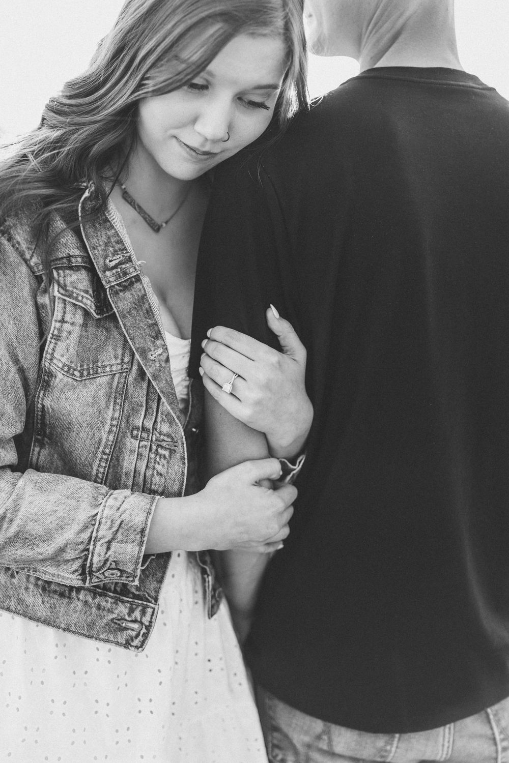 Black and white romantic shot showing a couple embracing, with soft lighting highlighting a denim jacket and white dress.