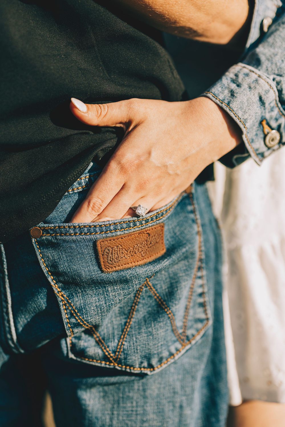 A hand with manicured nails slips into the back pocket of vintage Wrangler jeans showing the brown leather patch.