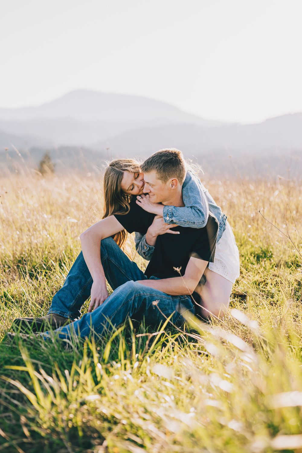 A romantic moment captured in tall grass with mountains in the distance during sunset.
