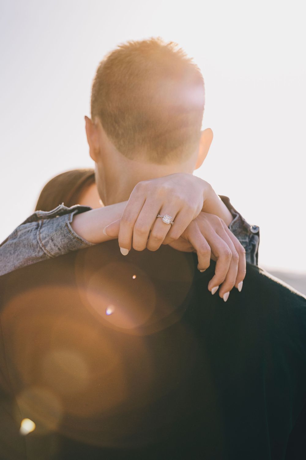 A romantic couple embraces in a backlit setting with sun flares and a wedding ring visible.