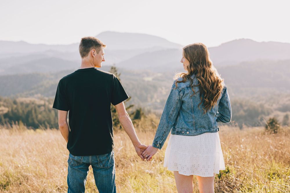 A couple holding hands while looking at scenic mountain views in golden sunlight.