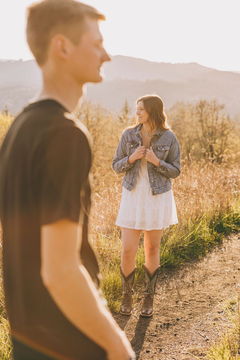 A couple shares a playful moment on a mountain trail during golden hour.