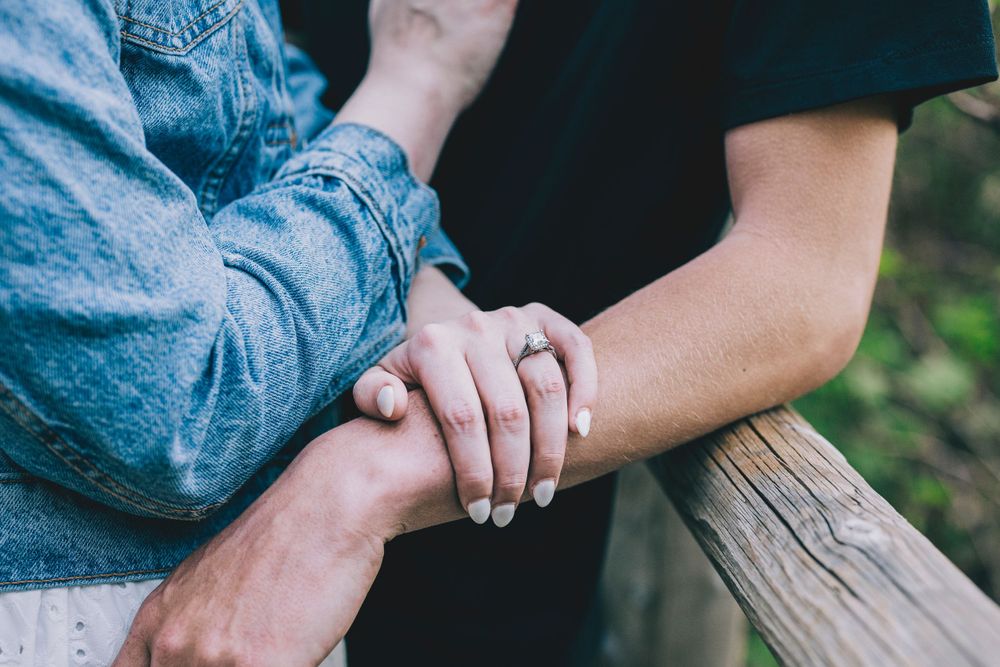 Close up shot of two hands clasped together showing engagement or wedding rings against denim clothing.