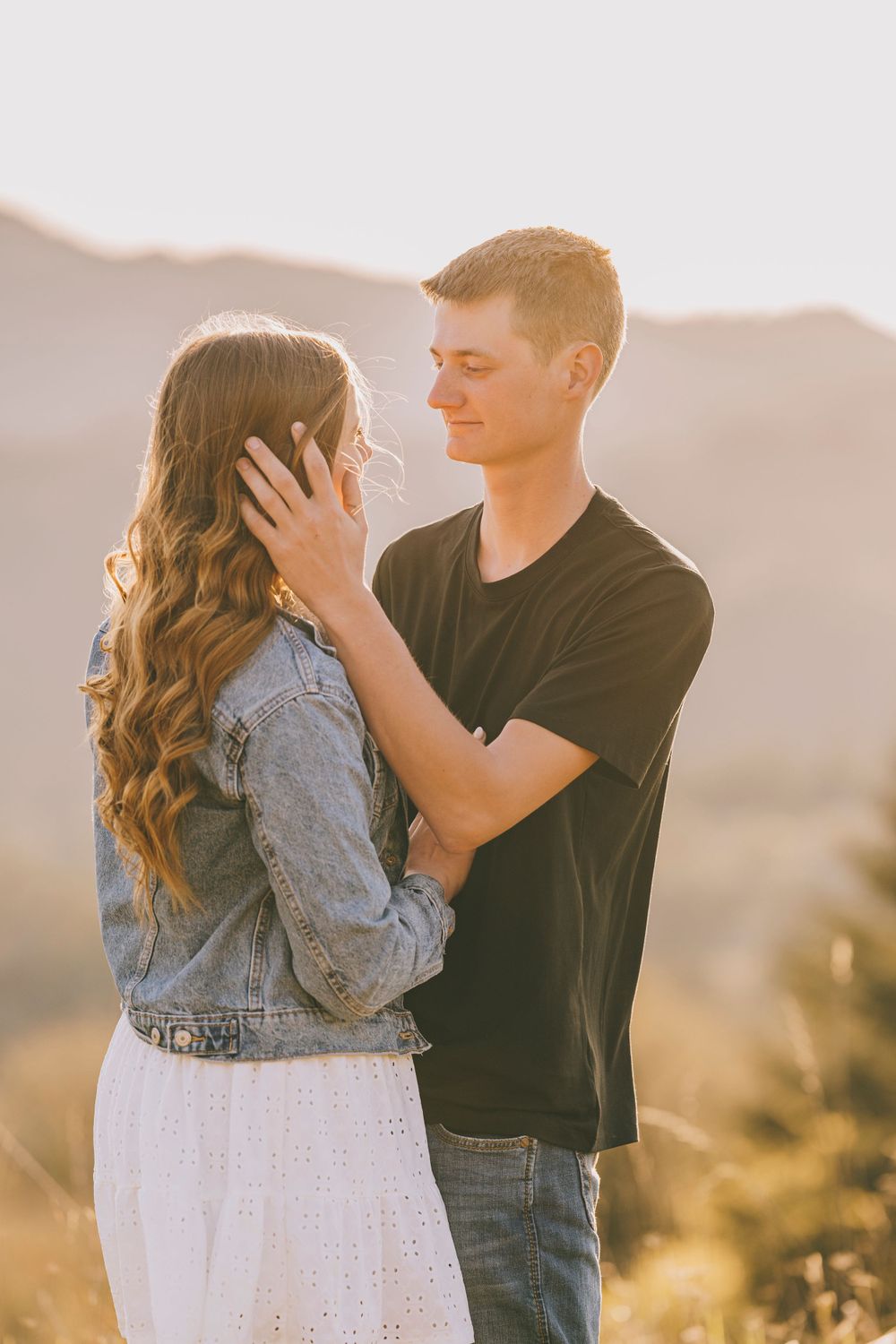 A tender moment between a couple backlit by golden sunset light in a mountainous setting.