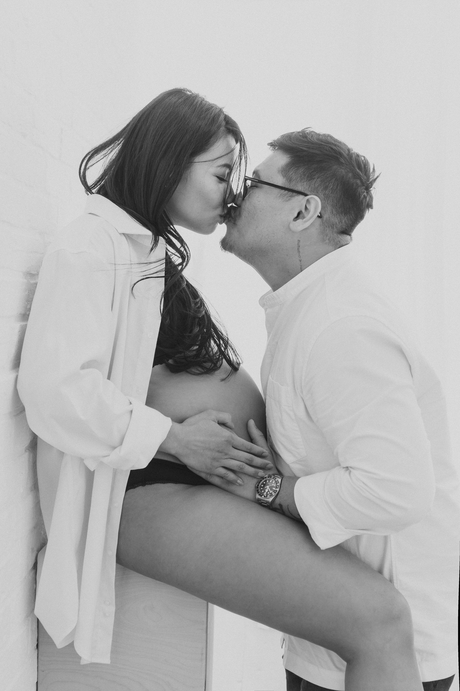 An intimate black and white portrait of a couple sharing a passionate kiss while wearing white shirts.