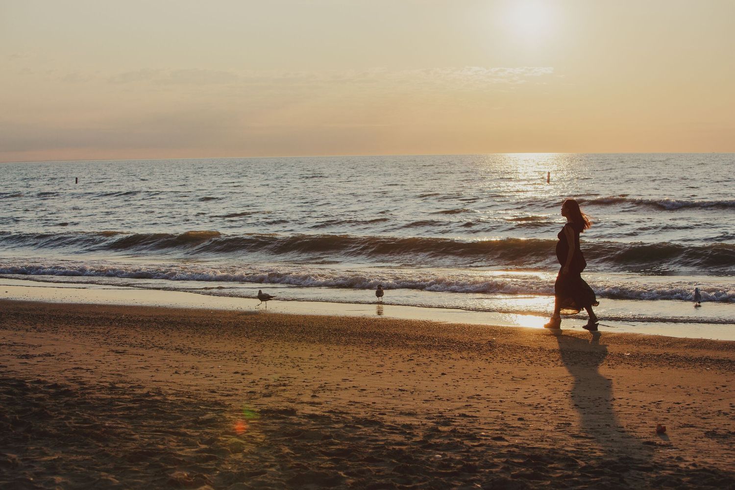Silhouette of person jogging along beach at sunset with waves crashing on shore and golden light reflecting off ocean.