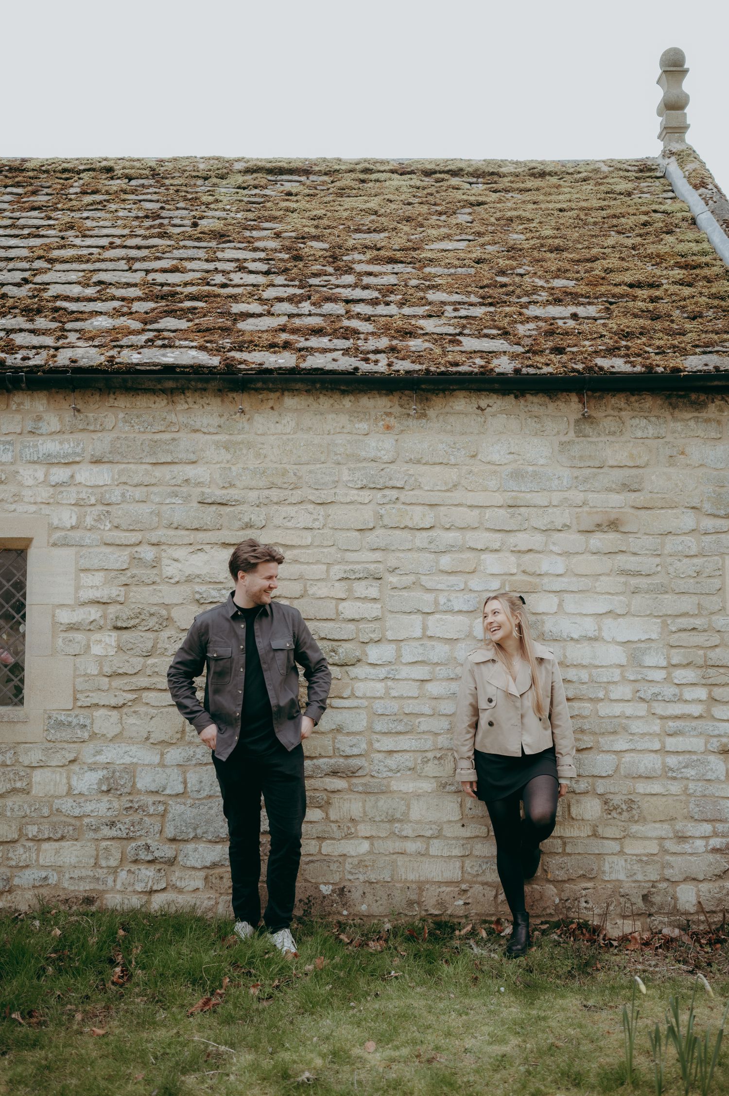 A casual outdoor photoshoot against a rustic stone wall and tiled roof.