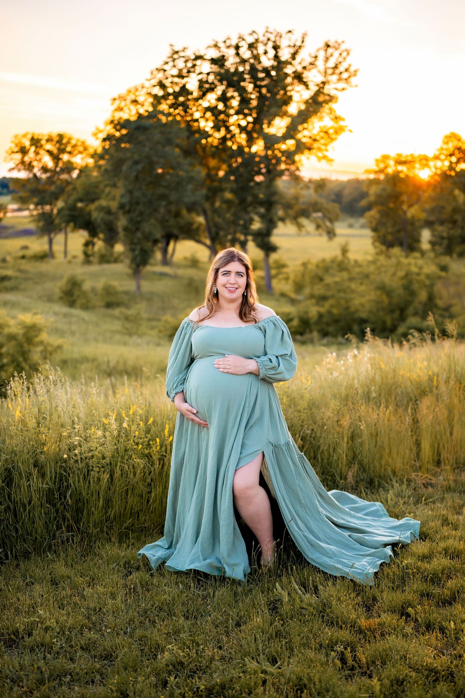 Ethereal maternity photoshoot in sage green flowing dress during golden hour sunset in a grassy meadow.