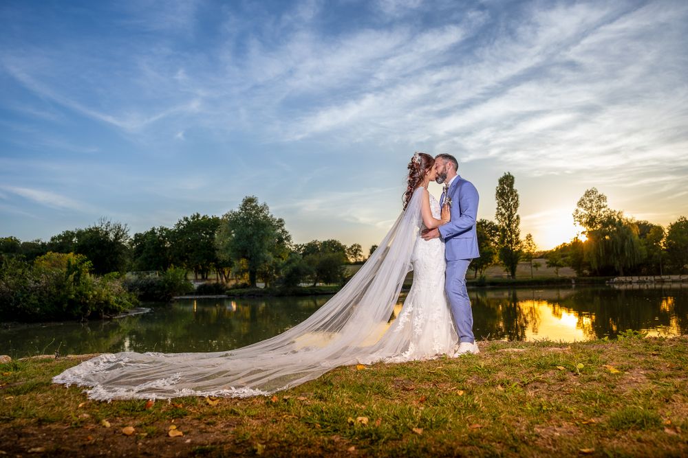 A romantic lakeside wedding photo with a long flowing veil during golden hour.