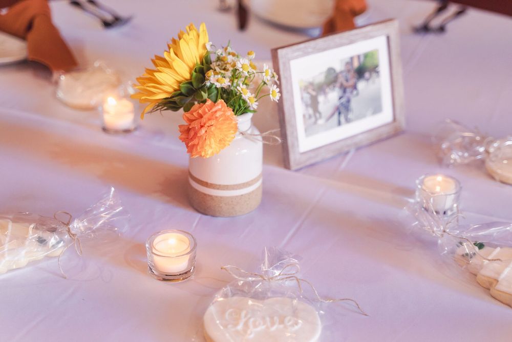 A simple photograph in a wooden frame and a ceramic vase with sunflowers and mums decorate this fall DIY wedding reception table.