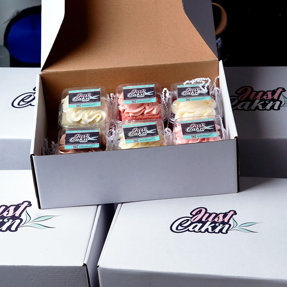 An open white shipping box containing individually wrapped protein cookies or snack bars arranged neatly in rows.