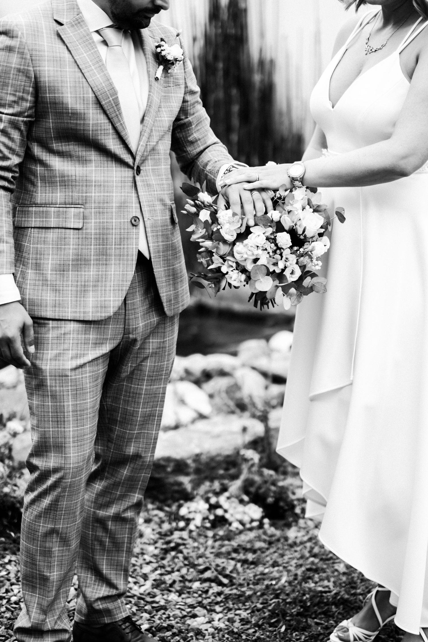 Black and white close-up of bride and groom's hands holding bouquet with floral details.