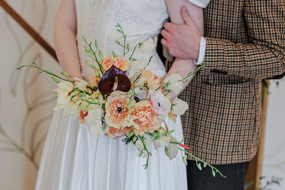 A delicate peach and cream wedding bouquet held against a white dress and plaid suit jacket.