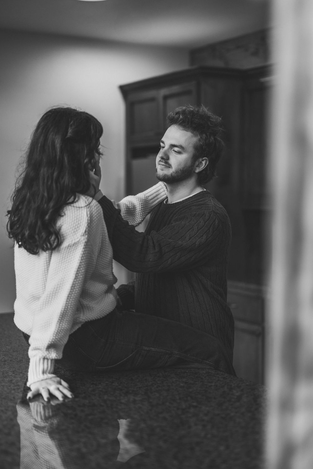A tender black and white photograph of a couple sharing an intimate moment together in a dimly lit room.