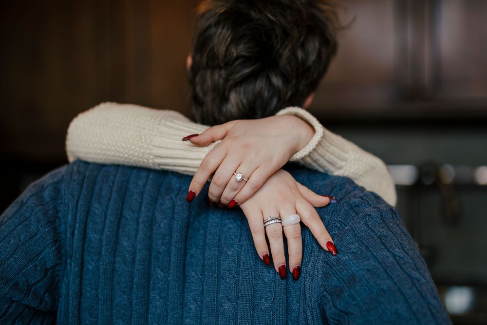 A close-up view of hands wearing a diamond ring resting on a blue knit sweater.