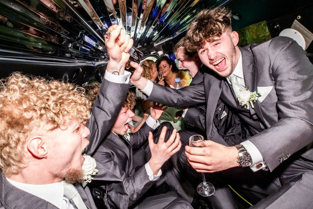 A group of excited party guests in suits celebrate with champagne glasses under dynamic lighting at a formal event.