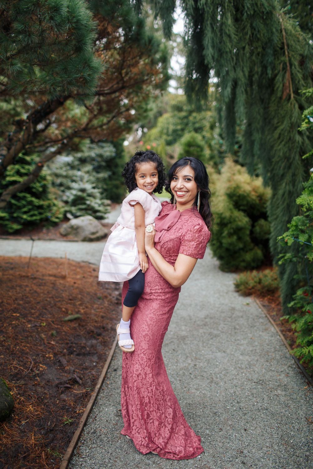 Seattle portrait photographer: A mother carrying her young daughter, both dressed in pink against a natural green backdrop in Washington