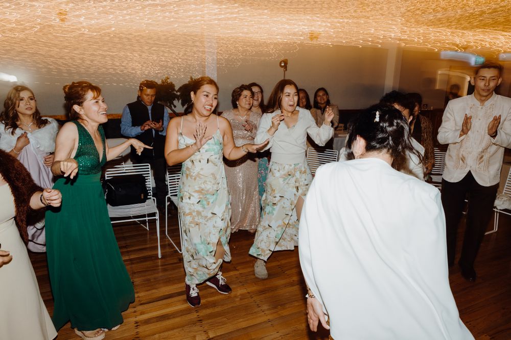Group of wedding guests dancing together on wooden floor at indoor celebration.
