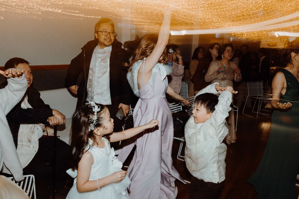 Party guests dance and celebrate on wooden dance floor at indoor reception.