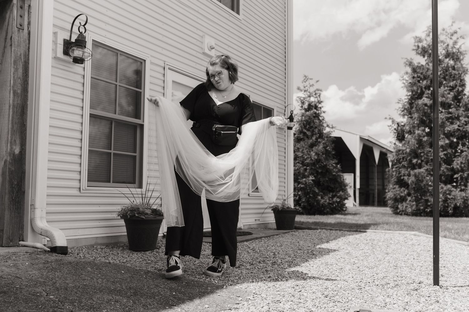Black and white photo of couple in playful pose outside white house.