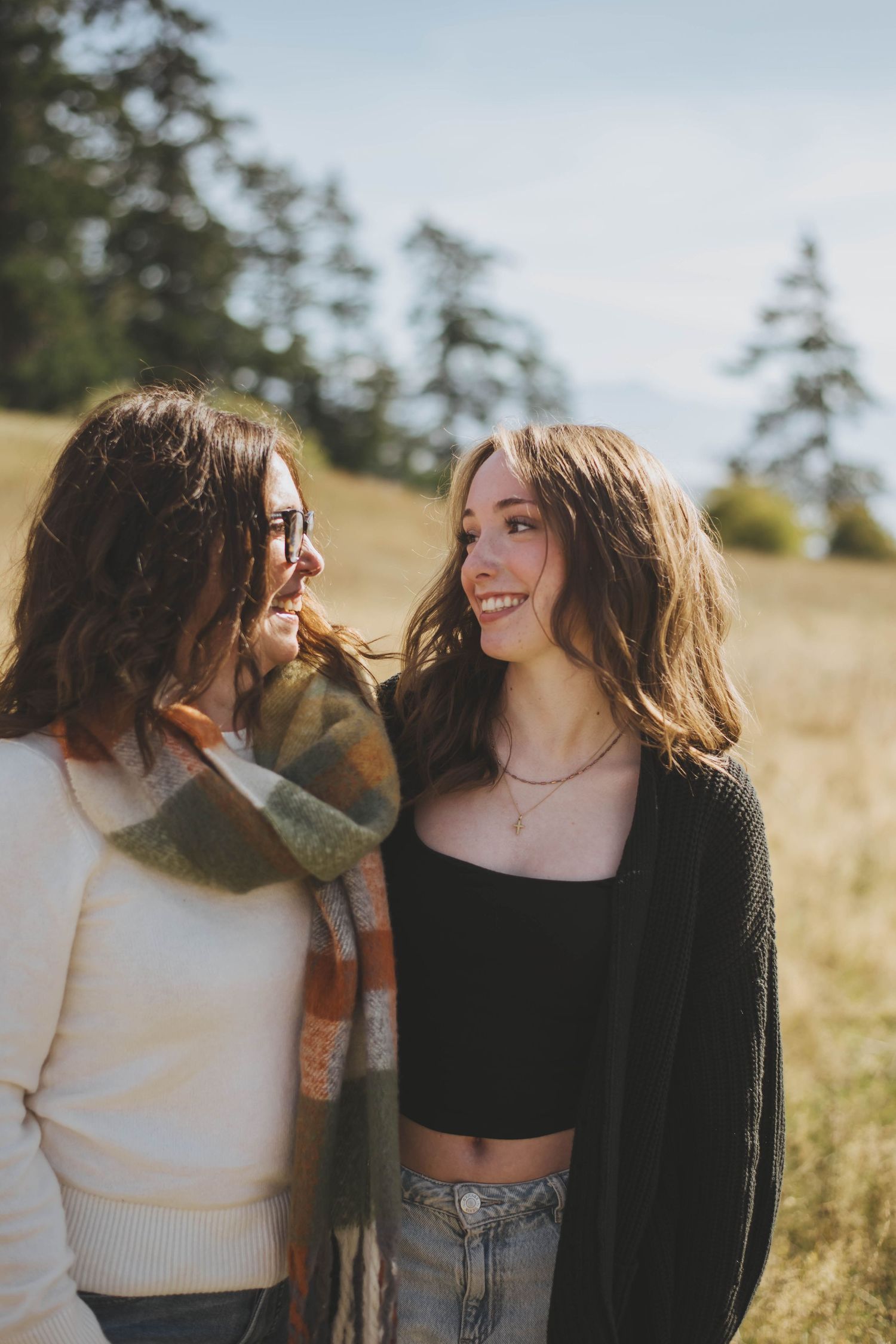A mother and daughter share a joyful moment, smiling at each other in a sunlit field, with soft light filtering through