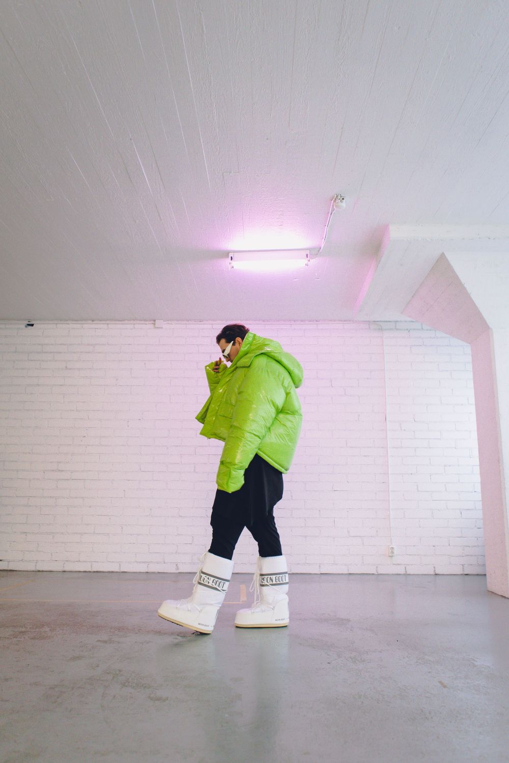 Person in neon green puffer jacket poses in white industrial space.