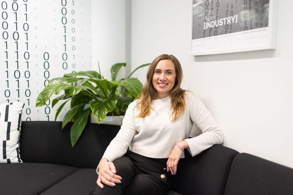 Professional sitting on a grey couch in a modern office with binary code wall art.