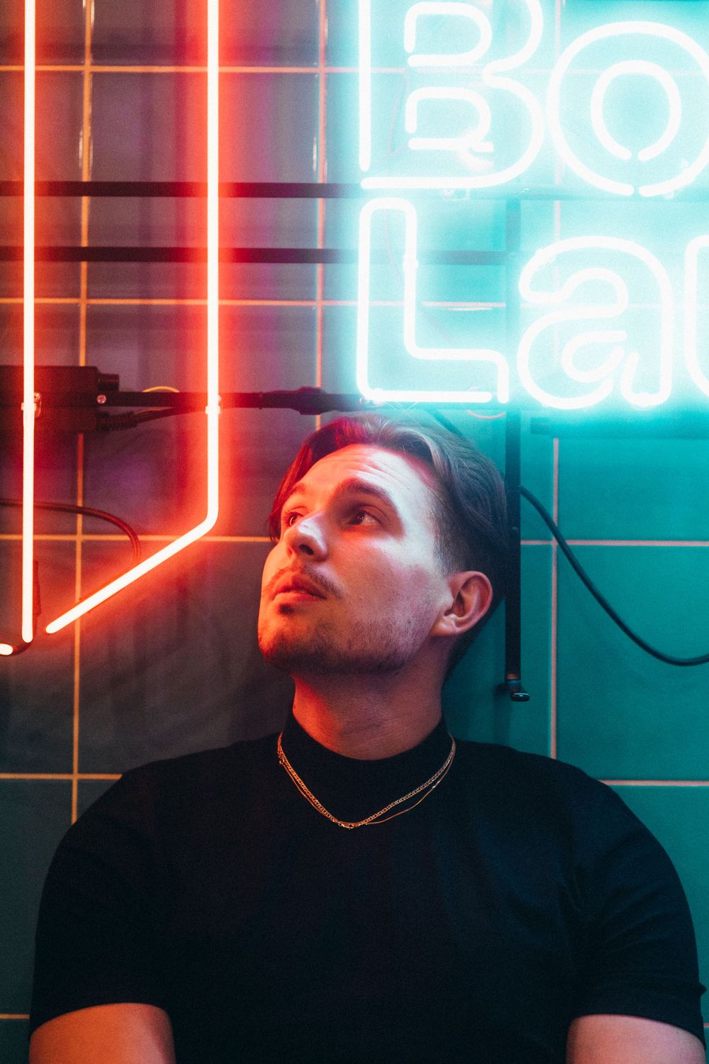 Portrait of person under neon lights against teal tiled wall.