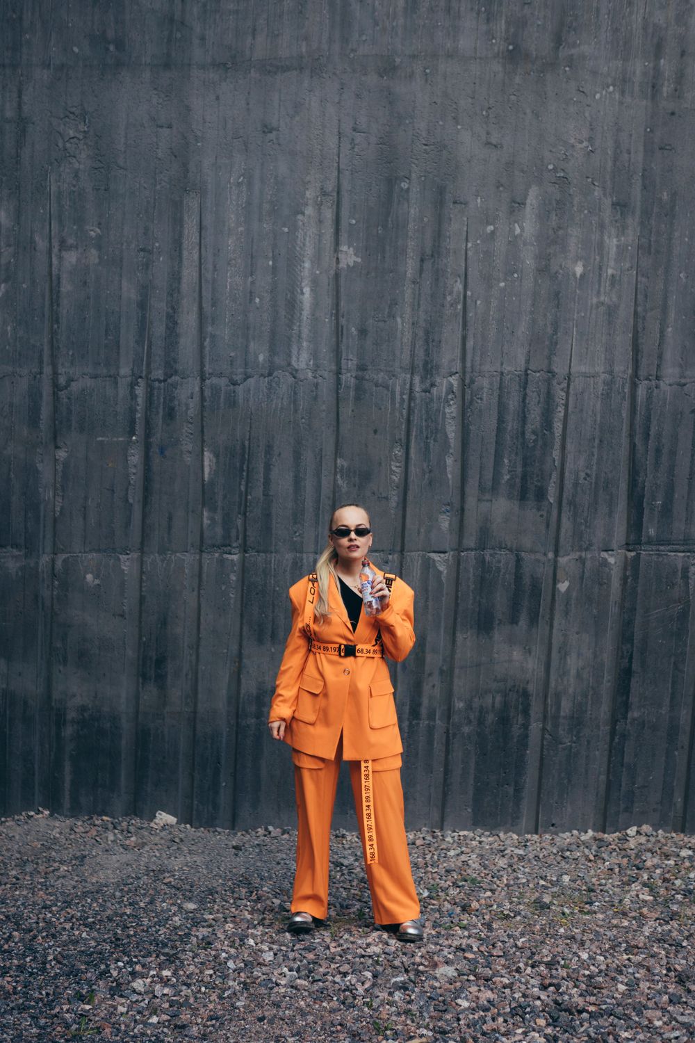 Person in bright orange suit standing against concrete wall outdoors.