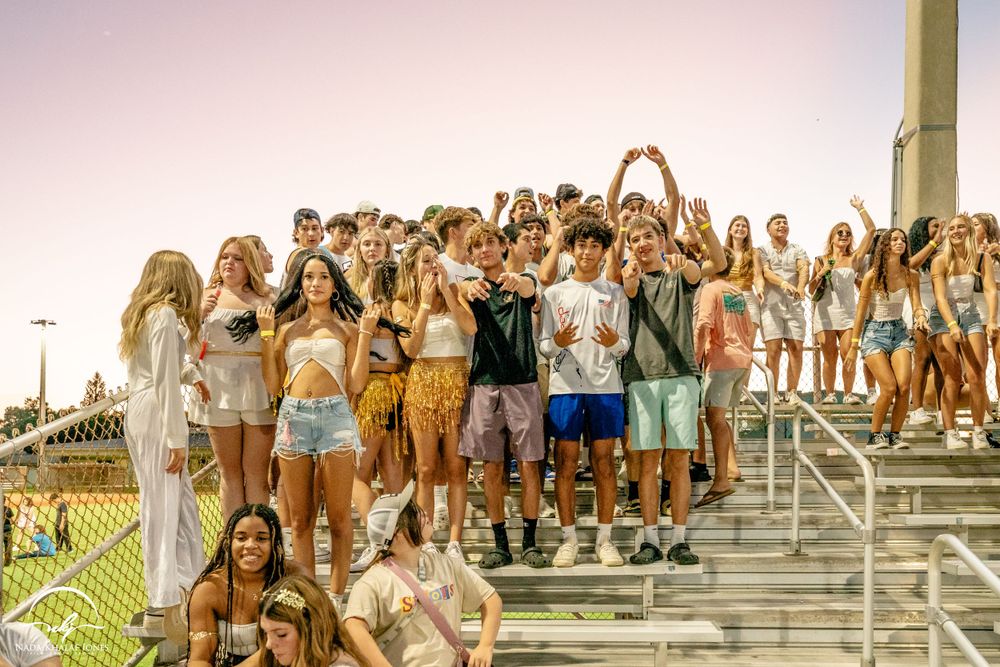 Large group of students cheering and celebrating together in outdoor stadium bleachers.
