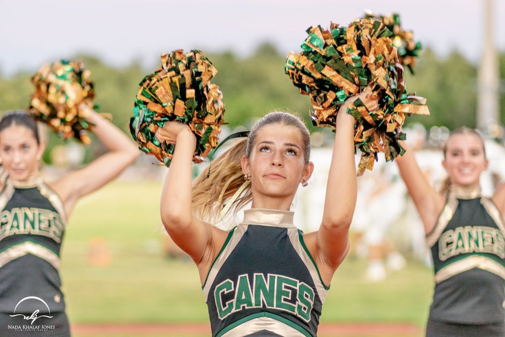 Cheerleader performing with orange and black pom poms during an outdoor sports event.