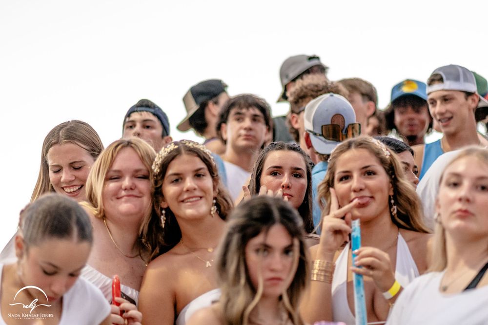 Excited crowd of students cheering in bleachers at an outdoor sporting event.