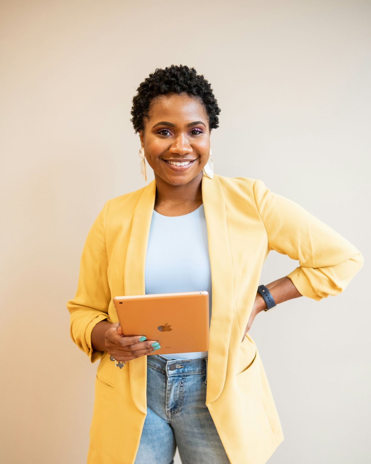 Modern professional in yellow blazer holding tablet with confident pose against neutral background.
