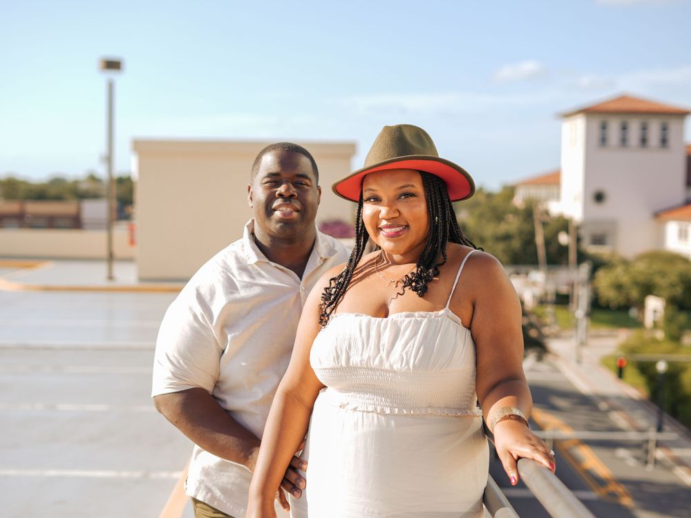 A couple poses together on a rooftop with urban architecture in the background.
