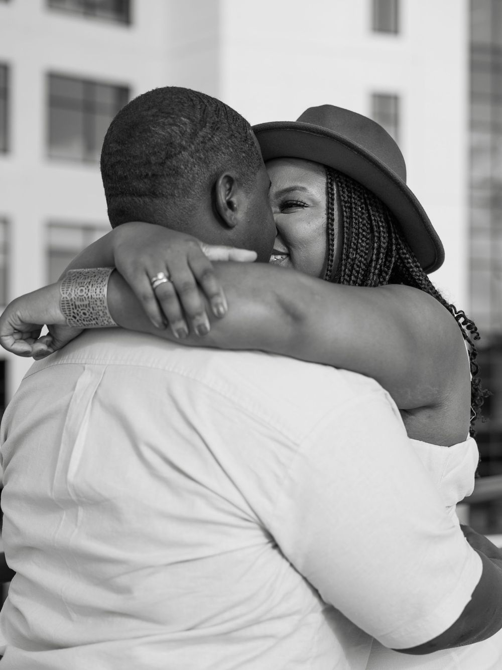 A tender embrace captured in black and white photography against an urban backdrop.