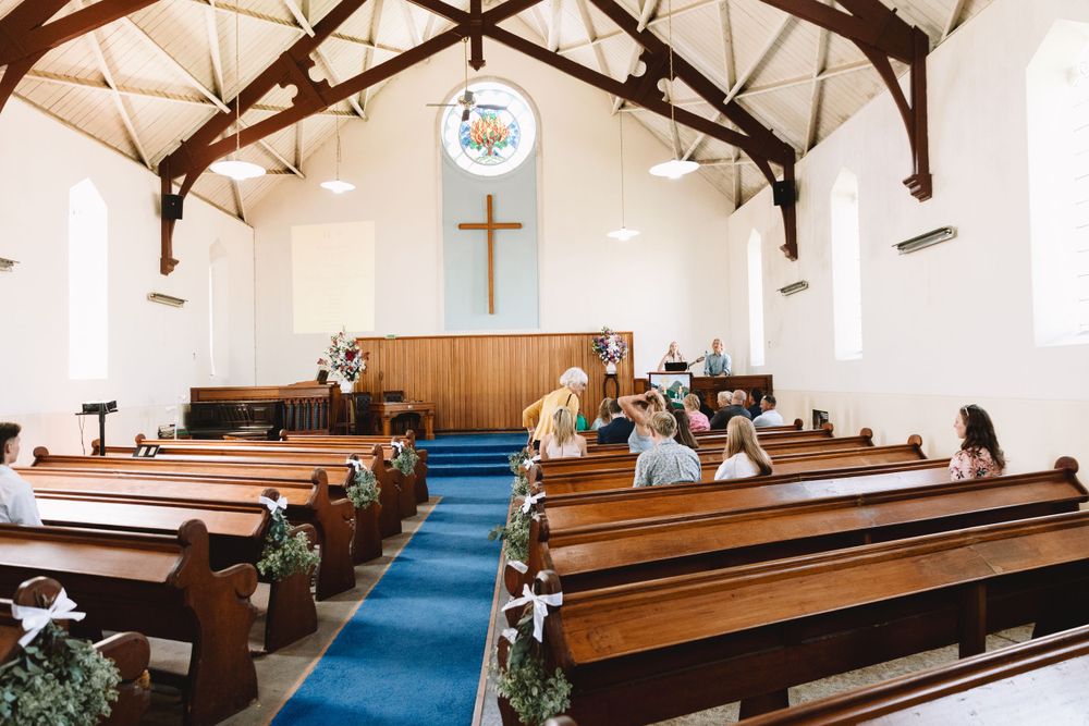 Church sanctuary with exposed wooden beams and pews decorated for a wedding ceremony.