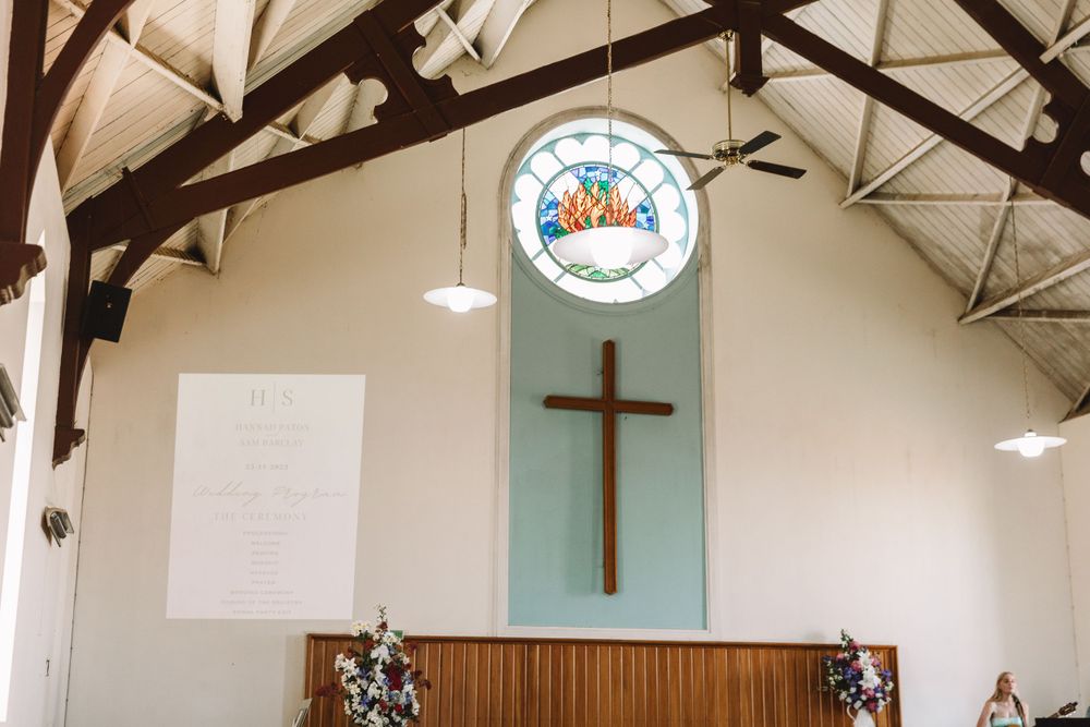 White church interior featuring a wooden cross and stained glass window on the altar wall.