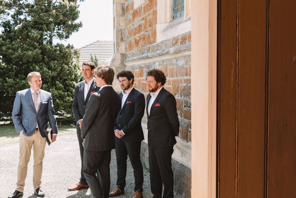 A small group gathers outside a stone church building in casual and formal attire.