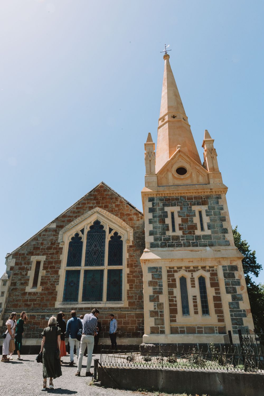 Gothic revival stone church with a tall spire and arched windows against a bright blue sky.