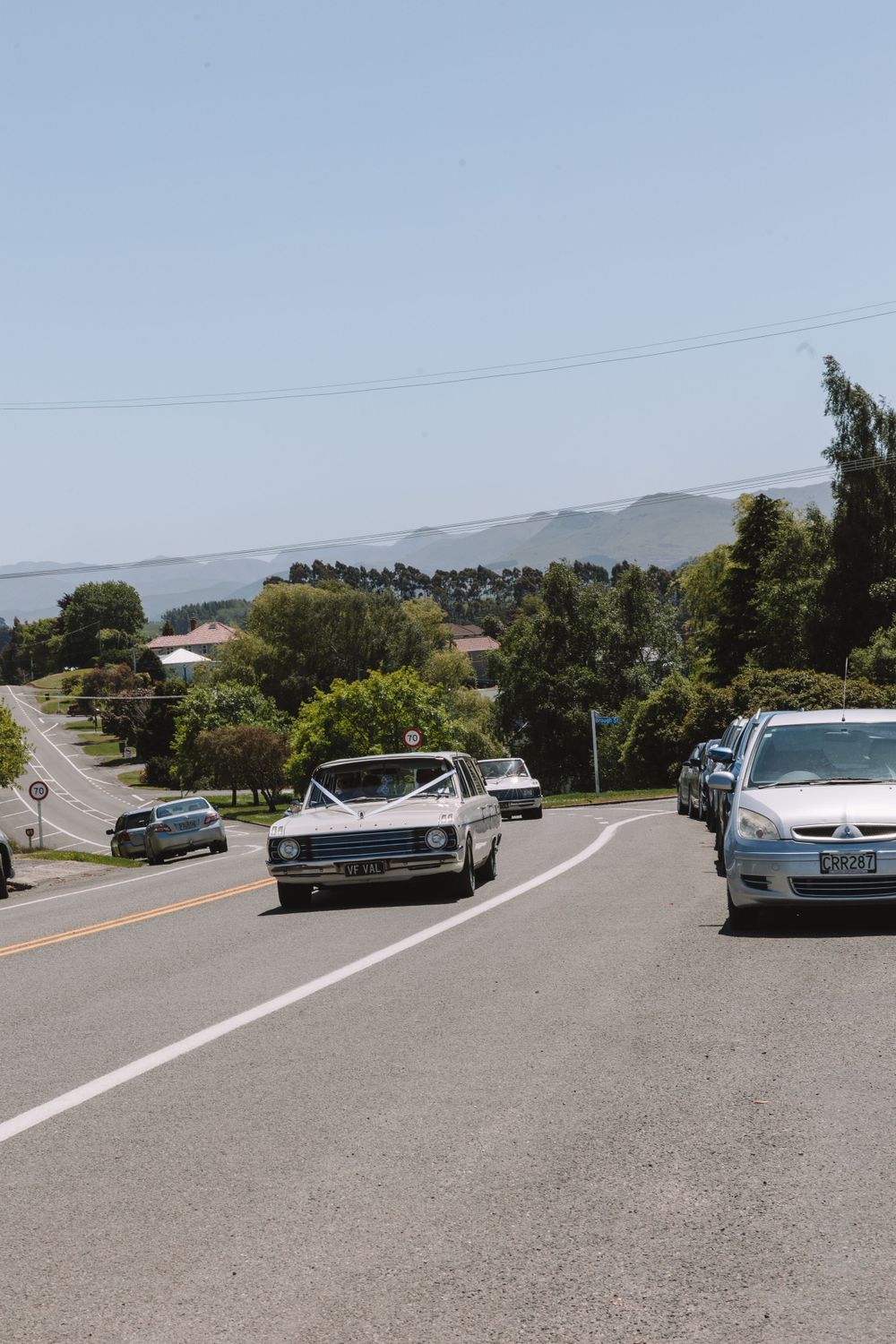Classic vintage car driving on a hillside road with mountain views.