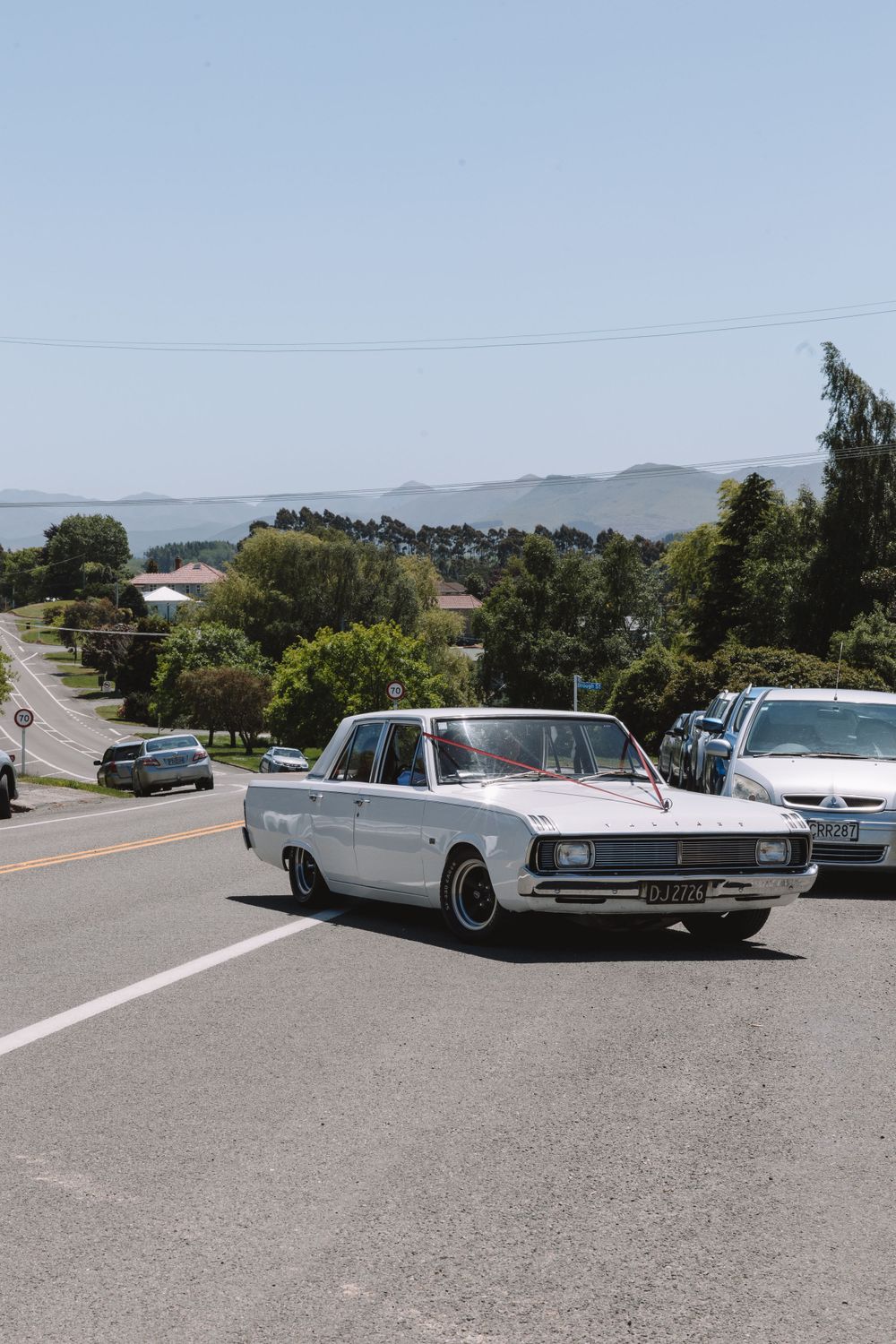 Vintage silver Chrysler sedan parked on a hilltop road with mountains in background.