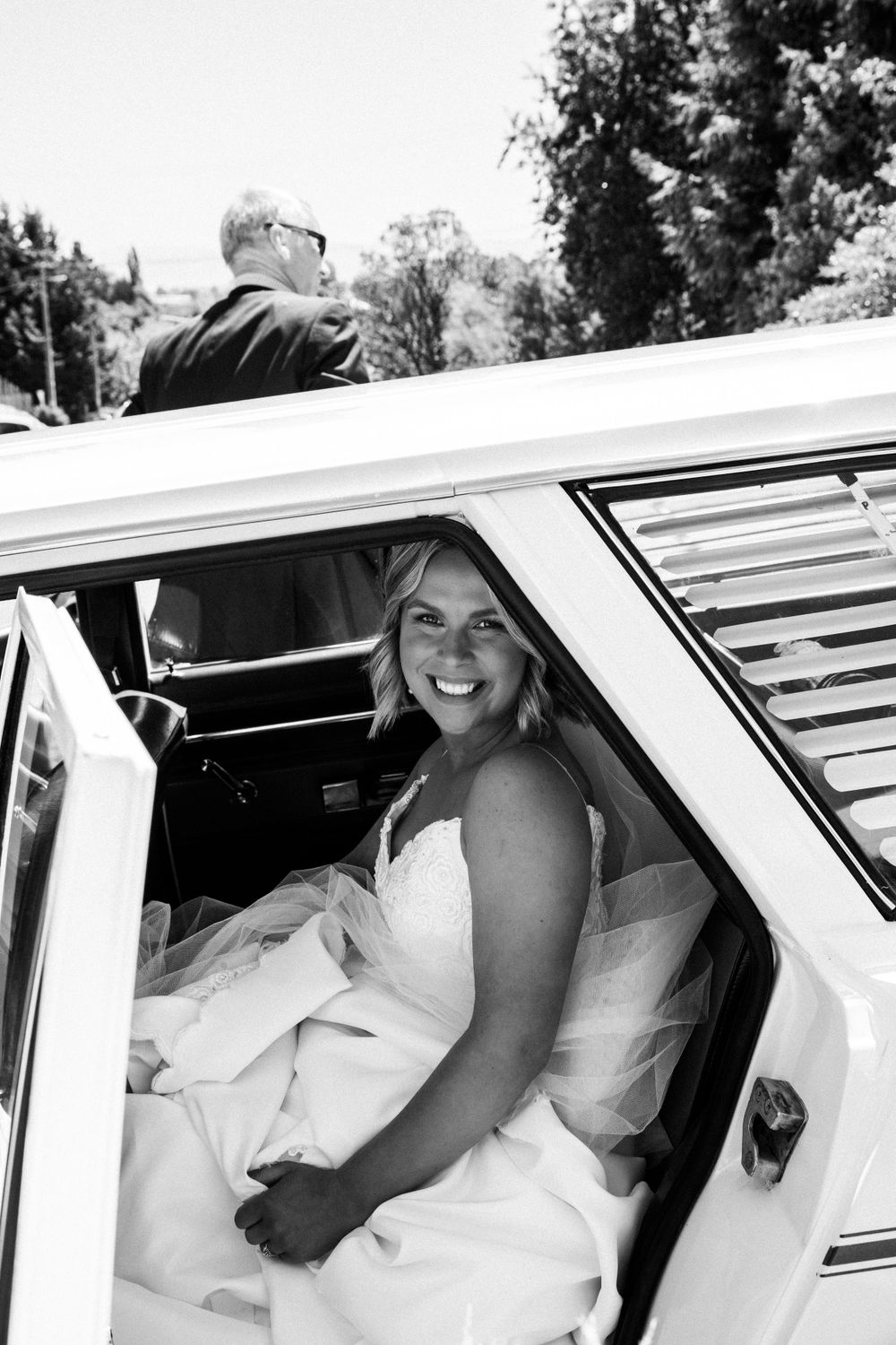 Passenger seated in vintage white wedding car with retro window louvers.