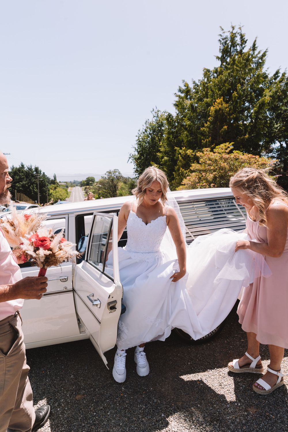 Wedding party helping with white dress near vintage car door.
