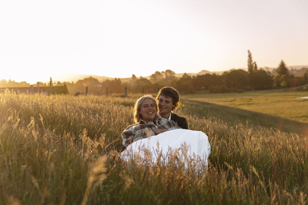 Wedding couple sharing intimate moment while seated in sunlit meadow at dusk.