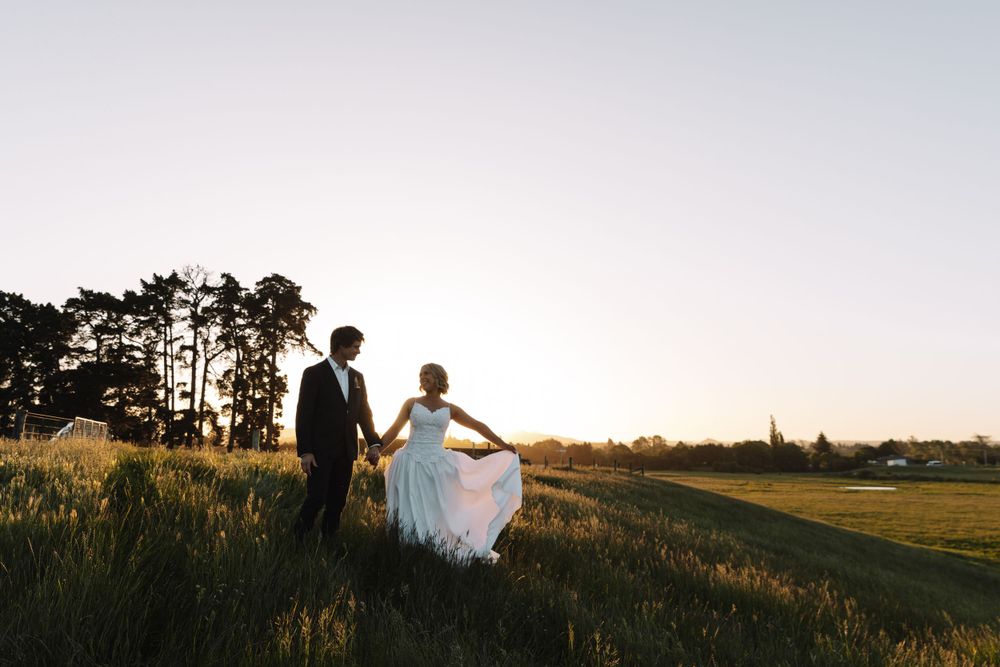 Newlyweds walking together on hillside with white dress flowing in evening light.