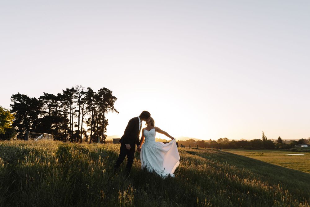 Dancing couple in formal attire twirl on hilltop during golden hour.